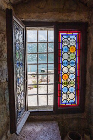 Téléchargez les photos : Vue à travers un joli vitrail à Notre-Dame des Rochers vers la baie de Kotor et les montagnes environnantes sur la côte monténégrine prise en mai 2023. - en image libre de droit