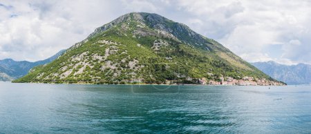Foto de Una de las montañas que bordea la bahía de Kotor se eleva por encima del bonito pueblo de Perast en Montenegro. - Imagen libre de derechos