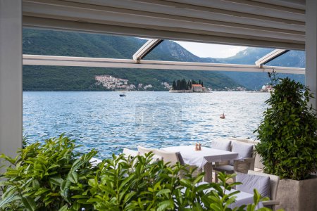 Foto de Mesas colocadas en el borde de las aguas en Perast con vistas a lo largo de la bahía de Kotor y los dos islotes. - Imagen libre de derechos