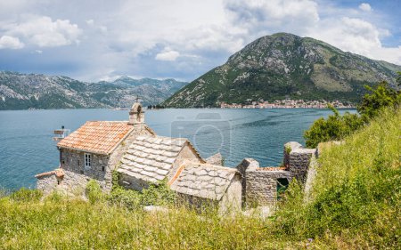 Photo for Our Lady of Angels or the Lepetani Orthodox Church seen protecting Perast in the distance in the Bay of Kotor in June 2023. - Royalty Free Image