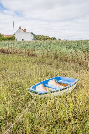 Photo for A lone boat tied to the shore at Brancaster Staithe pictured on long grass at low tide on the North Norfolk coast. - Royalty Free Image