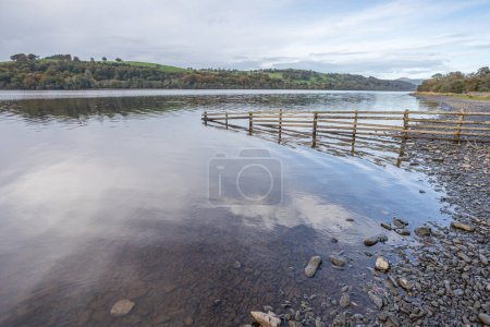 Photo for Pebbles line the shoreline of Lake Bala as a wooden fence dips into the water in Snowdonia National Park. - Royalty Free Image