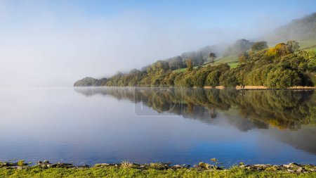 Photo for Reflections of trees and two men fishing on Lake Bala as the morning mist slowly lifts. - Royalty Free Image