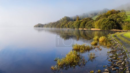 Photo for A multi image panorama of two men fishing on Lake Bala as the mist slowly lifts around them revealing stunning reflections in the water. - Royalty Free Image
