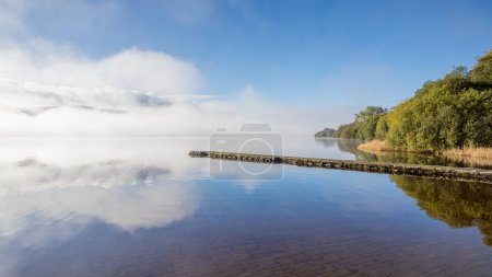 Photo for A view over the edge of Lake Bala over a concrete landing stage to the beautiful still water and the mountains as they peak from the low cloud. - Royalty Free Image