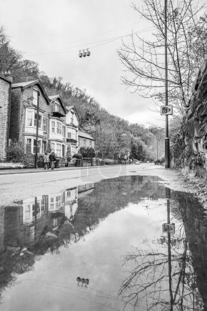 Three of the cable car cabins of the Heights of Abraham reflect in a puddle between the road and River Derwent in Matlock Bath, Derbyshire in April 2024.