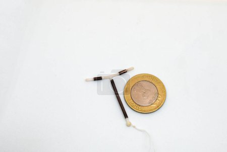 Photo for T shape IUD Gold hormon free birth control device beside a coin for size and shape realisation on white background. Selective focus. - Royalty Free Image