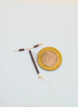 Photo for T shape IUD Gold hormon free birth control device beside a coin for size and shape realisation on white background. Selective focus. Vertical image. - Royalty Free Image