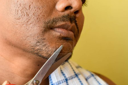 An Indian male grooming and beautifying his beard and mustache with a small scissors. Selective focus.