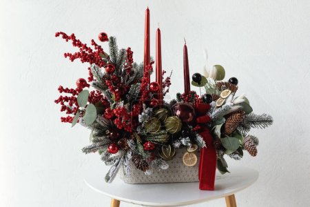 Téléchargez les photos : Arrangement traditionnel de fleurs de Noël de branches de sapin vert et de bougies rouges pour un cadeau. Décor du Nouvel An pour l'intérieur - en image libre de droit