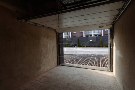 Ein offenes Tor zu einer leeren, geräumigen Garage in einem modernen Ferienhaus
