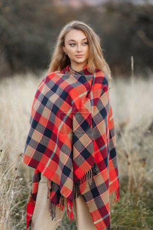 Foto de Beautiful girl covered with a red blanket in an apple orchard at sunset - Imagen libre de derechos