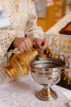 Téléchargez les photos : Consecration of water. The priest's hand touches the water in the wooden Church before the christening the baby. - en image libre de droit
