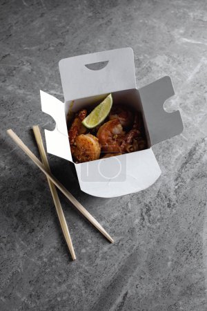 Photo for Chinese food in a black takeout box on a gray background. Sushi chopsticks and a black box. - Royalty Free Image