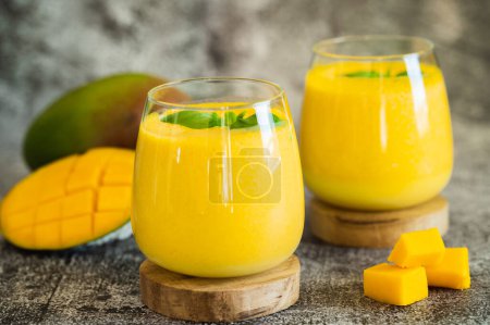 Fresh mango lassi in glasses on grey background with copy space. Indian healthy detoxic ayurvedic cold drink with mango. Freshness lassi made of yogurt, water, spices, fruits and ice