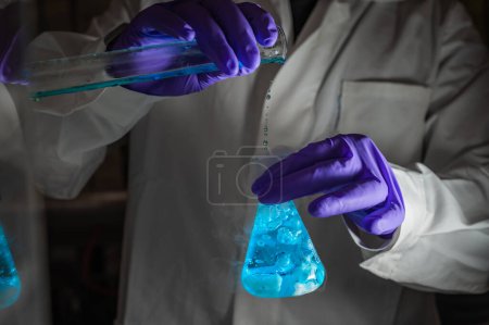 Téléchargez les photos : Un chercheur scientifique expérimentant une gouttelette fluorescente verte dans une fiole conique en verre dans un laboratoire biomédical sombre pour le développement de la médecine des soins de santé. Espace de copie fond noir - en image libre de droit