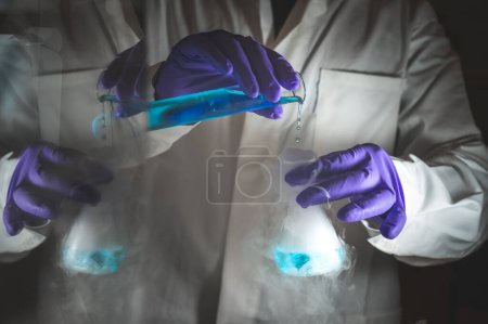 Téléchargez les photos : Expériences fumées avec des gouttelettes bleues. Scientifique travaillant sur la réaction chimique, générant une épaisse fumée à partir d'une fiole de verre. Espace de copie - en image libre de droit