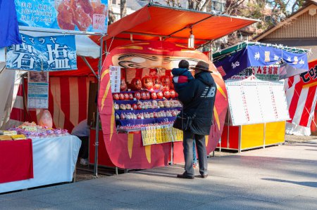 Photo for Chiyoda City, Tokyo, Japan - January 03, 2020: Father with son on his lap looking at Daruma dolls on display at a sales stand. - Royalty Free Image
