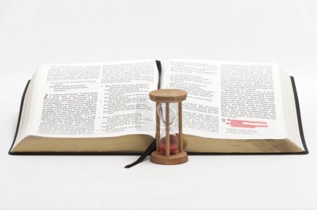 Sanduhr und aufgeschlagene Bibel im Buch Prediger mit selektivem Fokus auf Vers 1 des dritten Kapitels rot hervorgehoben. Isoliert auf weißem Hintergrund.
