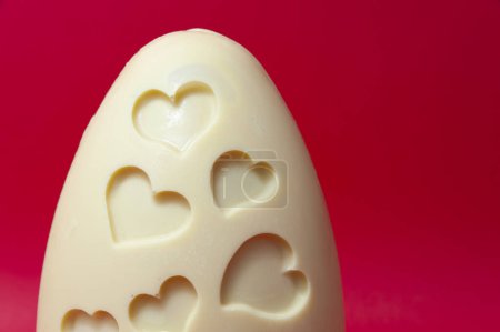 Köstliche und originelle hausgemachte weiße Schokolade Osterei mit Herzformen verziert isoliert auf lebendigem roten Hintergrund.