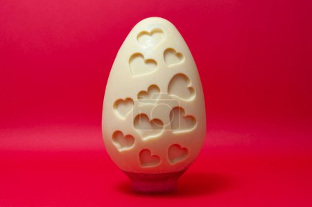 Delicioso y original chocolate blanco casero Huevo de Pascua decorado con formas de corazón aislado sobre fondo rojo vivo.