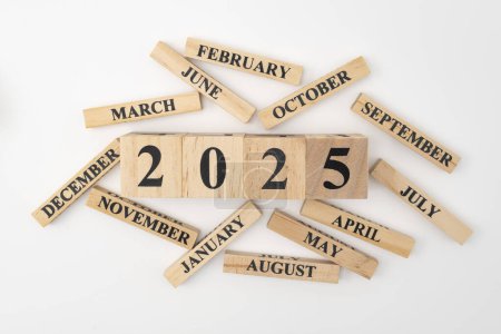 Blocs et cubes en bois avec l'année 2025 et les 12 mois de l'année éparpillés au hasard autour. Isolé sur fond blanc.