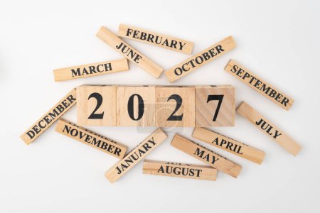 Wooden blocks and cubes with the year 2027 and the 12 months of the year randomly scattered around. Isolated on white background.
