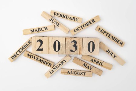 Blocs et cubes en bois avec l'année 2030 et les 12 mois de l'année éparpillés au hasard autour. Isolé sur fond blanc.