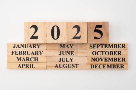 Année 2025 écrite sur des cubes de bois au-dessus des mois de l'année écrite sur douze morceaux rectangulaires de bois. Isolé sur fond blanc.