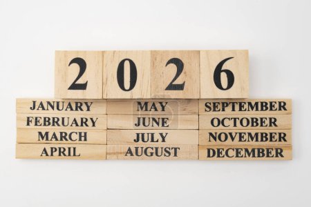 Jahr 2026 geschrieben auf Holzwürfeln über den Monaten des Jahres geschrieben auf zwölf rechteckigen Holzstücken. Isoliert auf weißem Hintergrund.