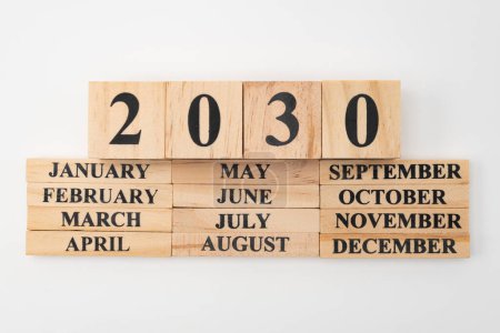 Année 2030 écrite sur des cubes de bois au-dessus des mois de l'année écrite sur douze morceaux rectangulaires de bois. Isolé sur fond blanc.