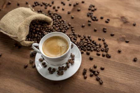 Foto de Una taza de café caliente en una mesa rústica de madera y un saco lleno de granos de café. - Imagen libre de derechos
