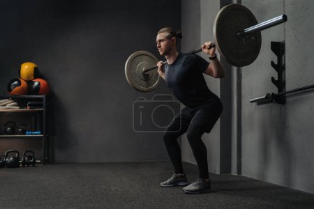 Téléchargez les photos : Homme haltère de levage dans le cadre de l'entraînement crossfit dans la salle de gym d'entraînement sombre. Espace pour le texte - en image libre de droit
