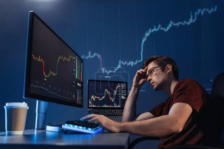 Crypto trader investor looking at computer screen with candlestick chart late night, thinking about global risks of online stock exchange market, upset with global recession and loss of money