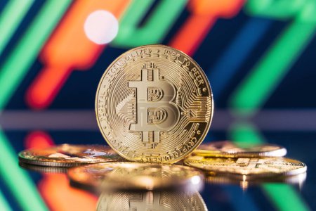 Téléchargez les photos : Golden bitcoin standing on mirror surface reflecting blurred background with crypto chart with green and red candlesticks. Cryptocurrency trading market concept - en image libre de droit