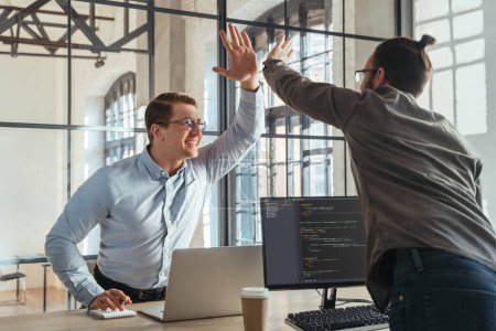Téléchargez les photos : Colleagues coders giving high five to each other celebrating successful start-up launch. Programmers rejoice at the successful launch of their product. - en image libre de droit
