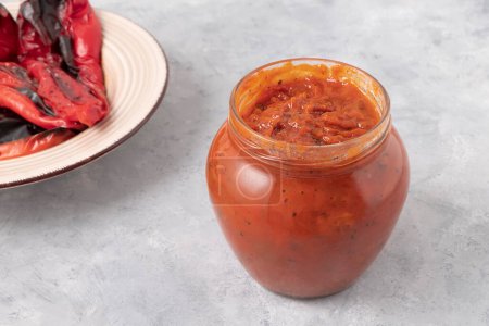 Glass jar of delicious Ljutenica made of roasted bell peppers on neutral grey background. Balkan food