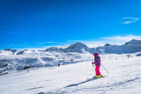 Foto de Young kid, girl skiing down on a ski slope. Sunny day on ski winter holidays in Andorra, El Tarter, Pyrenees Mountains - Imagen libre de derechos