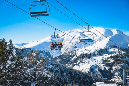 Foto de People riding up on a ski chair lift with snow capped mountains in the background. Winter holidays in Andorra, El Tarter, Pyrenees Mountains - Imagen libre de derechos