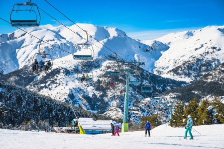 Foto de People riding up on a ski chair lift and skiing and snowboarding down on the ski slope. Winter holidays in Andorra, El Tarter, Pyrenees Mountains - Imagen libre de derechos