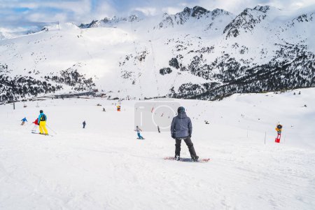 Photo for Snowboarders and skiers riding down the mountain towards valley below with snow capped mountain peaks in background, Andorra, Pyrenees - Royalty Free Image