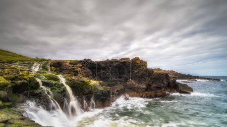 Foto de Dunseverick Falls con pequeños acantilados y vetas de agua que caen al Océano Atlántico, Costa de Calzada, Condado de Antrim, Irlanda del Norte - Imagen libre de derechos