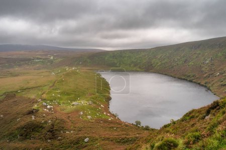 Foto de Lago, Lough Bray con sendero de montaña a la izquierda y acantilados a la derecha, cubierto de nubes de tormenta malhumoradas y dramáticas. Senderismo en Wicklow Mountains, Irlanda - Imagen libre de derechos