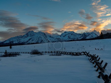 Snow and pole fence lead to a beautiful sunset over mountain range