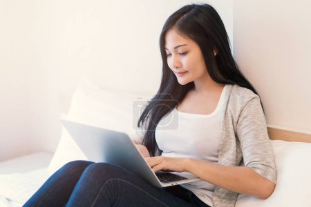 Young woman working on a laptop sitting on bed at home. Poster 650477202