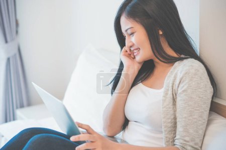 Young woman working on a laptop sitting on bed at home. Poster 650477212