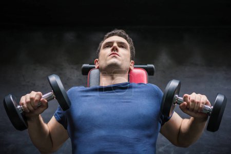 Foto de Guapo levantador de pesas levantamiento de pesas press ejercicio con mancuerna en el gimnasio - Imagen libre de derechos
