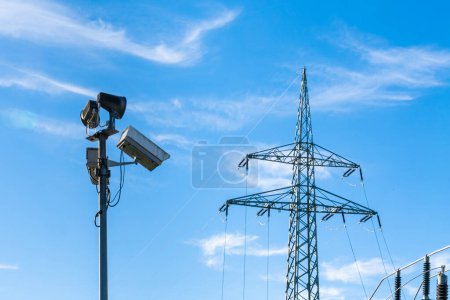 Téléchargez les photos : Caméras de surveillance sur un poteau et un mât de ligne haute tension contre le ciel bleu. - en image libre de droit