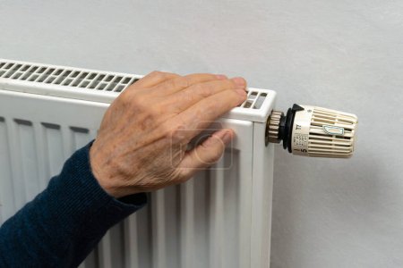 The hand of an elderly person is heated on a home heating radiator. Close up.
