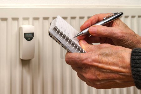 Photo for Man's hands recording heat consumption readings on a heating radiator. Close up. - Royalty Free Image